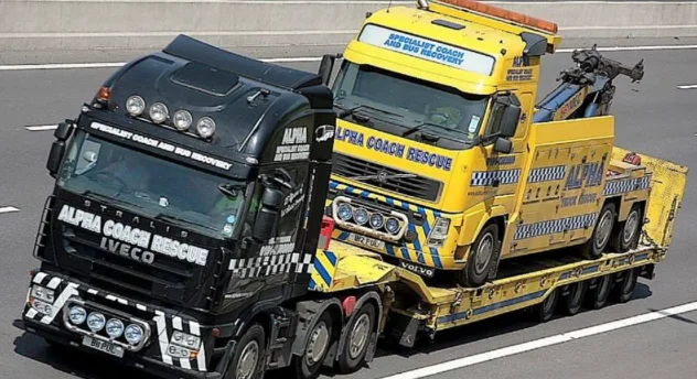 black tow truck transporting a large yellow tow truck