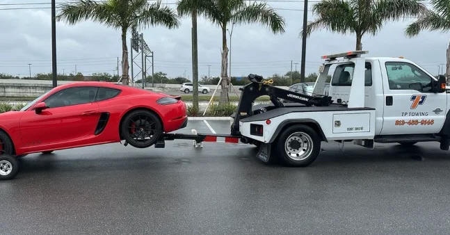 Tow truck towing a red sports car on a wet road.