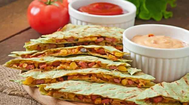 Mexican quesadilla sliced with vegetables and sauces on the table