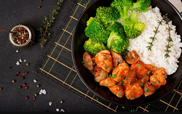 Pieces of chicken fillet with mushrooms stewed in tomato sauce with boiled broccoli and rice