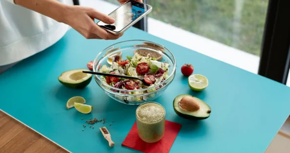 Female hands taking photo of a bowl with salad and half of avocado