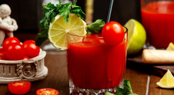 A glass of tomato juice garnished with cherry tomato lemon and parsley