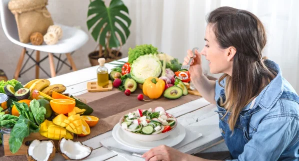 Young and happy woman eating salad at the table