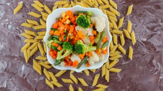 White bowl of fresh vegetables salad and raw penne on marble surface-inexpensive pasta recipes