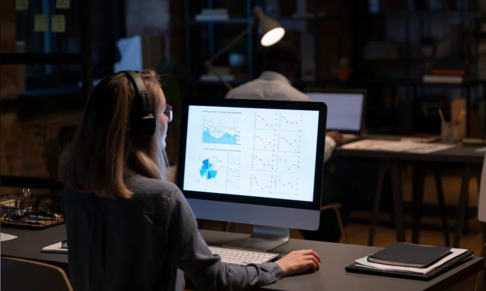 Female analyst reviewing website performance charts on desktop computer in office.