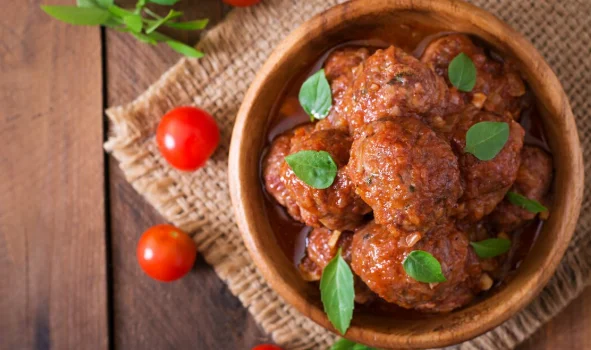 Meatballs in sweet and sour tomato sauce and basil in a wooden bowl
