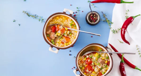 Soup with small pasta, vegetables and pieces of meat in bowl on blue table-slow cooker meals for two