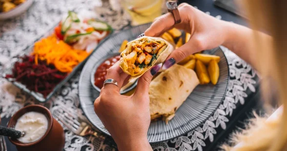 Woman holding chicken shawarma in flatbread served with fries sauces yogurt and pickles-easy family dinners