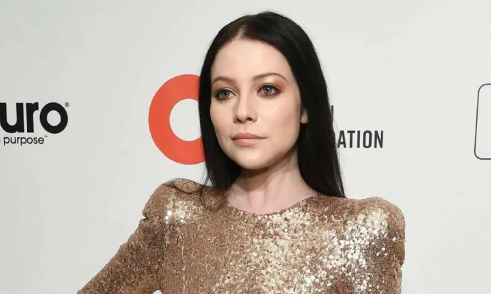 person with long dark hair wearing a glittering gold dress-michelle trachtenberg net worth