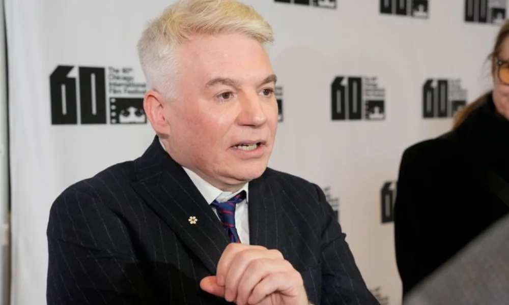 person with short blond hair and wearing a dark pinstripe suit