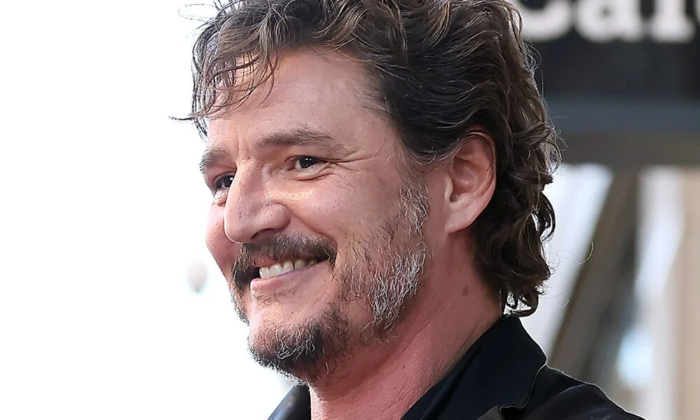  Pedro Pascal smiling in a close-up portrait while wearing a black shirt. 