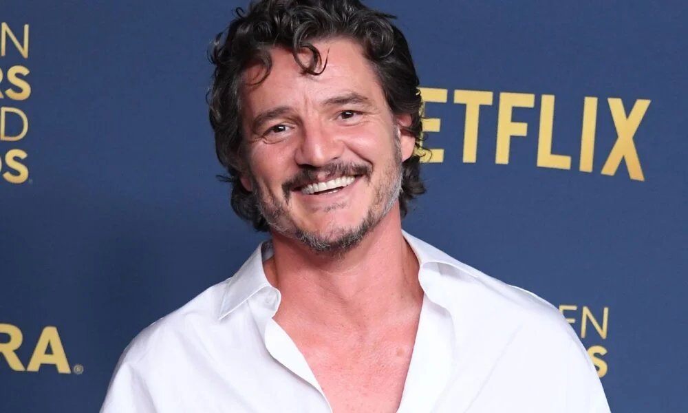 Pedro Pascal smiling in a white shirt at a Netflix event.