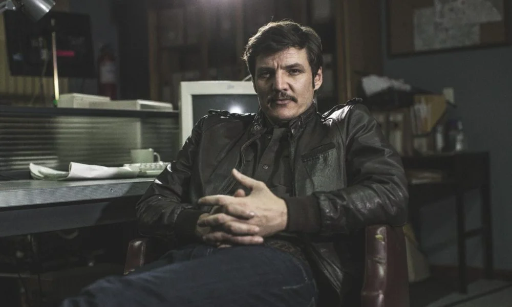 Pedro Pascal sitting in a dimly lit diner wearing a black leather jacket.
