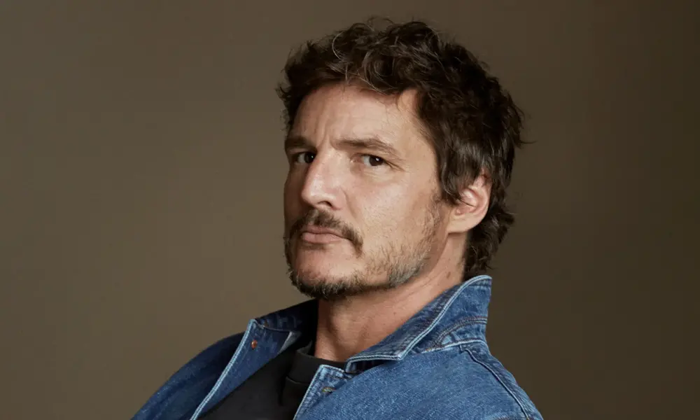 Pedro Pascal posing in a blue denim jacket against a neutral background.