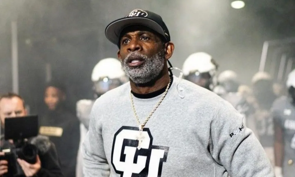  Deion Sanders in a gray Colorado sweatshirt leading his team onto the field.