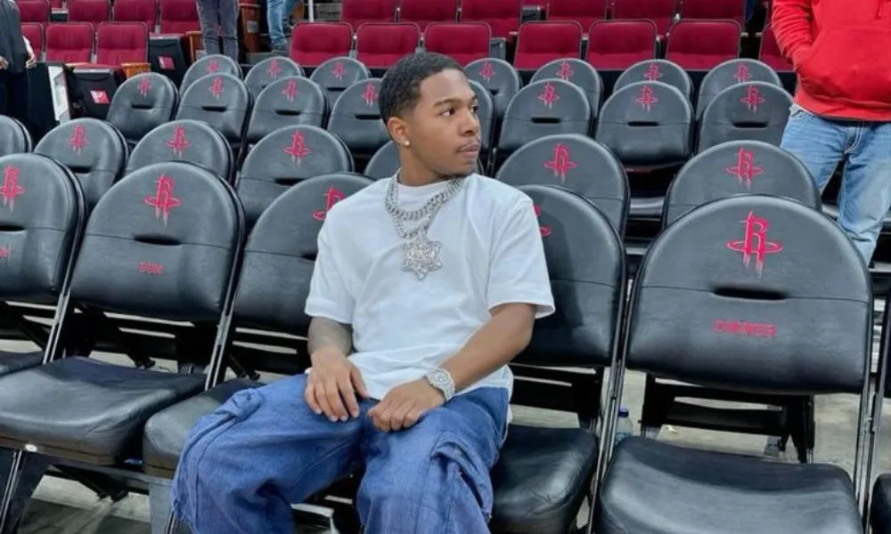 Deshae frost net worth 2026 highlights his success as an actor and content creator, seen here courtside at a basketball game in a white tee and baggy cargo jeans.