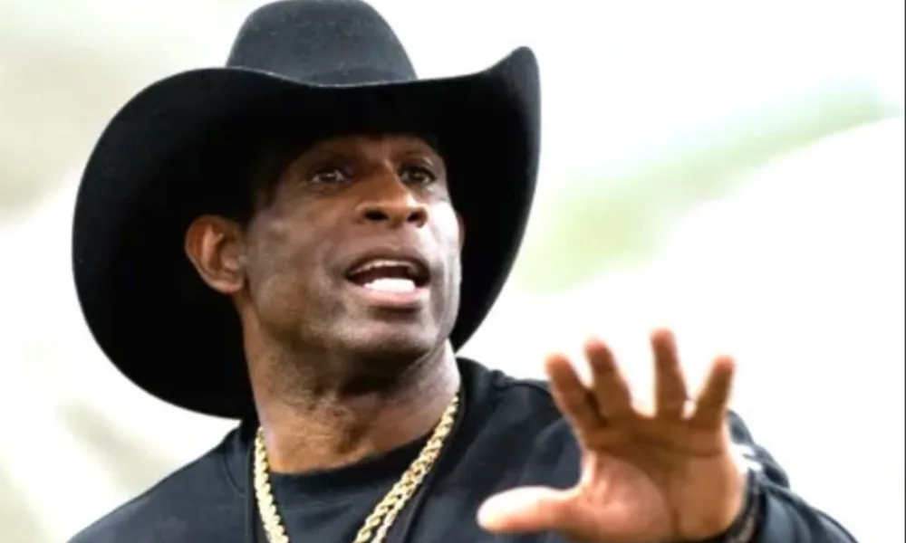  Deion Sanders in a black cowboy hat gesturing during an interview. 
