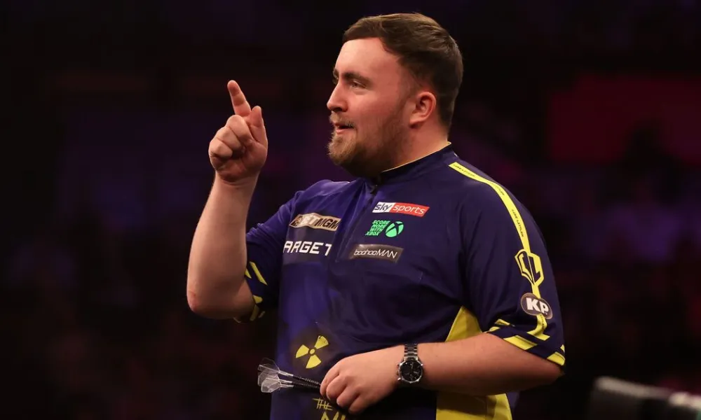  Darts phenom Luke Littler gestures to the crowd during a tournament match, illustrating his rapid rise to prominence and the growth of Luke Littler net worth. 