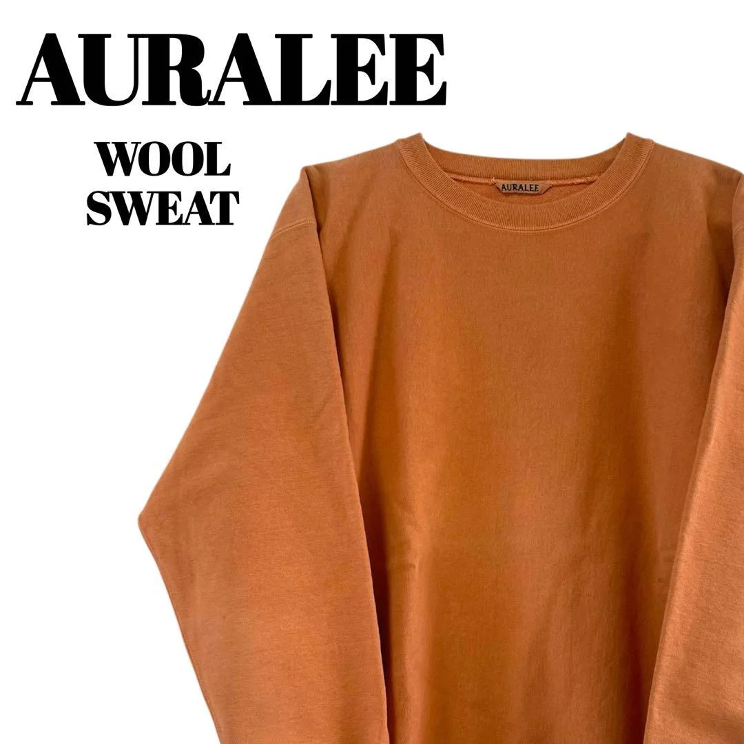 Rust-orange long-sleeved crewneck sweater with the text "AURALEE WOOL SWEAT" displayed on the left.