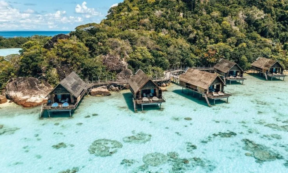 Overwater wooden bungalows nestled along the rocky coast of Bawah Reserve with crystal-clear turquoise waters and lush tropical foliage, representing one of thebest private island resorts