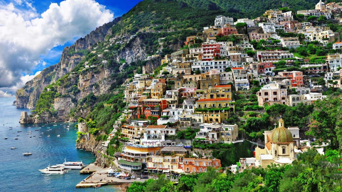 Colorful cliffside village of Positano on Italy's Amalfi Coast overlooking blue waters dotted with boats.