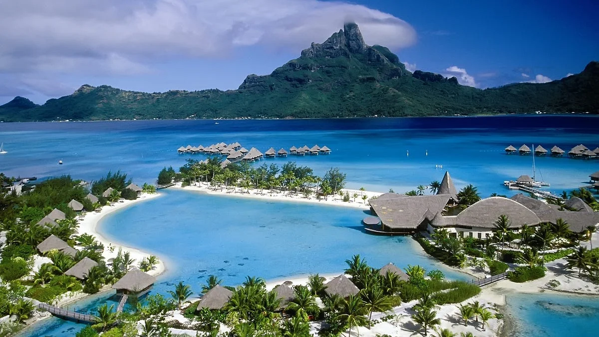 Overwater bungalows surrounding a clear turquoise lagoon with Mount Otemanu rising in the background of Bora Bora.