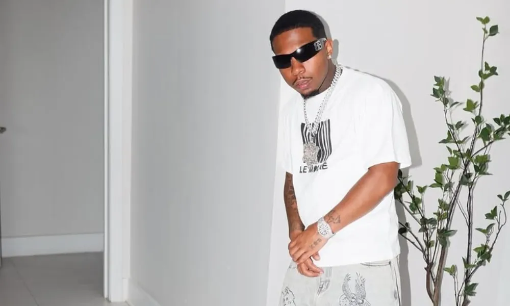 Deshae Frost in a stylish casual outfit wearing sunglasses, a white graphic tee, and printed jeans indoors featuring dashae frost nwt worth 2026.