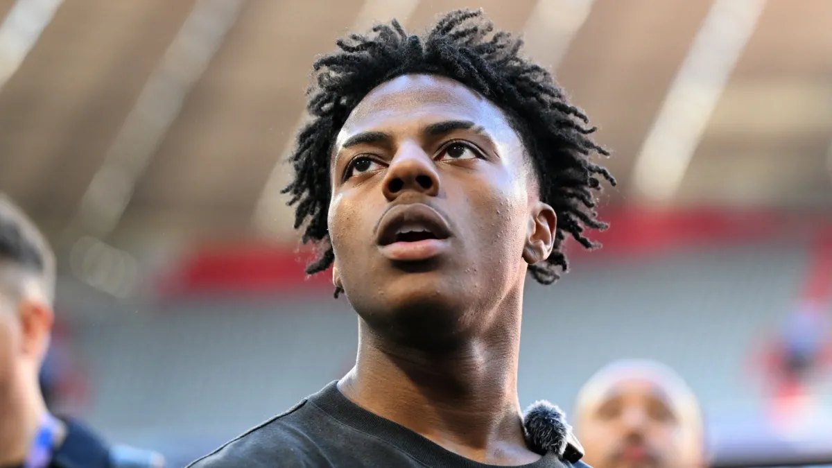 Close-up portrait of YouTuber IShowSpeed looking upward while wearing a black shirt and a lapel microphone inside a stadium venue.