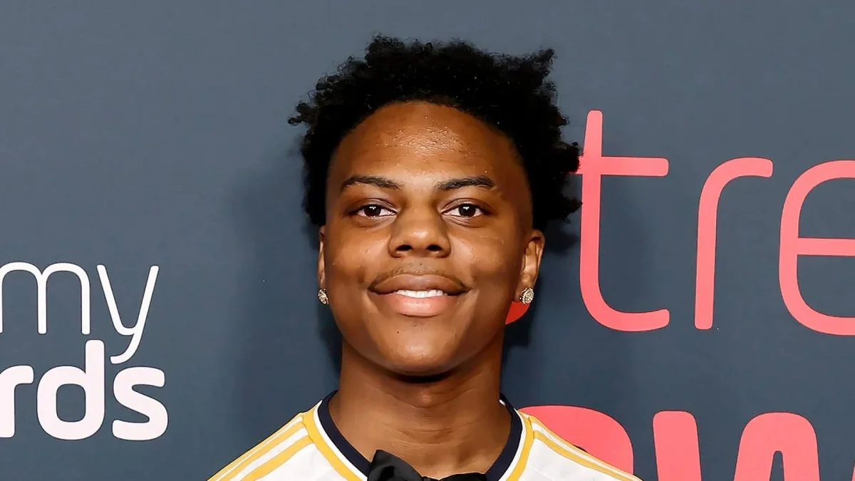 Streamer IShowSpeed smiling in a white and yellow sports jersey on a red carpet event backdrop.