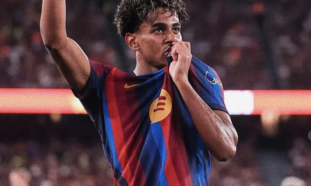 Young FC Barcelona winger Lamine Yamal kissing the team crest on his jersey while raising his arm in celebration during a match, perfect for an article covering lamine yamal net worth.