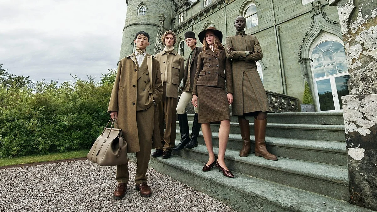 Five models posing outdoors in earth-toned high-fashion tailoring and leather boots on the stone steps of a European estate castle.