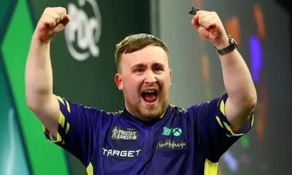 Wearing his sponsored darts jersey, Luke Littler cheers jubilantly after scoring, context directly tied to discussions around Luke Littler net worth and endorsements. 