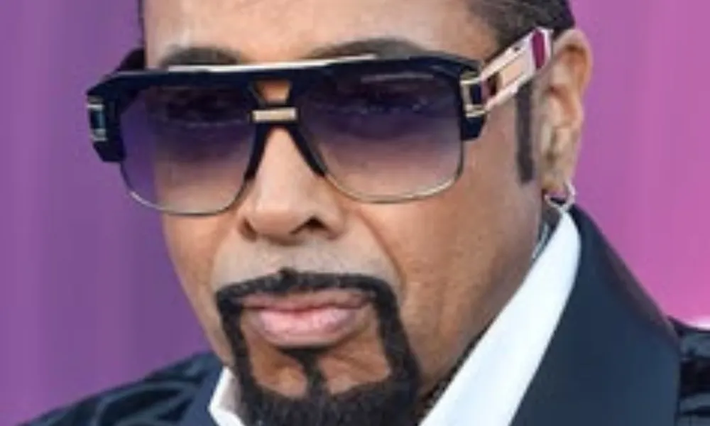 Morris Day Net Worth featured in a portrait of the musician wearing oversized dark sunglasses and a patterned lapel jacket.