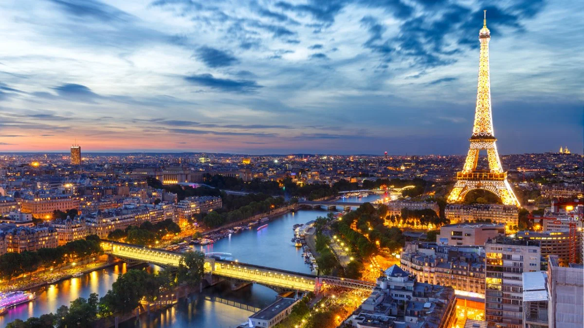 Illuminated Eiffel Tower and the Paris skyline along the Seine River at twilight.