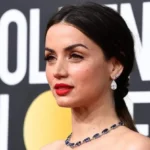 Ana de Armas net worth at the Golden Globe Awards wearing red lipstick, a braided hairstyle, drop earrings, and a sapphire necklace.