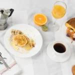 An overhead view of sandwich; pancake; juice; fruits