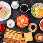 breakfast with fruits, toasts, cornflakes, yogurt on black surface