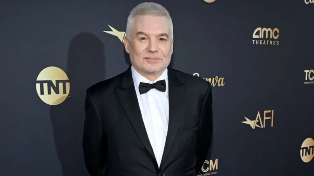 man in a tuxedo stands smiling against a dark backdrop