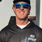 Cleetus McFarland Net Worth featured in a photo of a smiling Garrett Mitchell wearing blue sunglasses and a Cleetus McFarland hoodie outdoors.