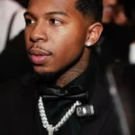 Deshae frost net worth 2026 reflects his successful career, pictured here wearing a black suit with a diamond chain at a formal event.