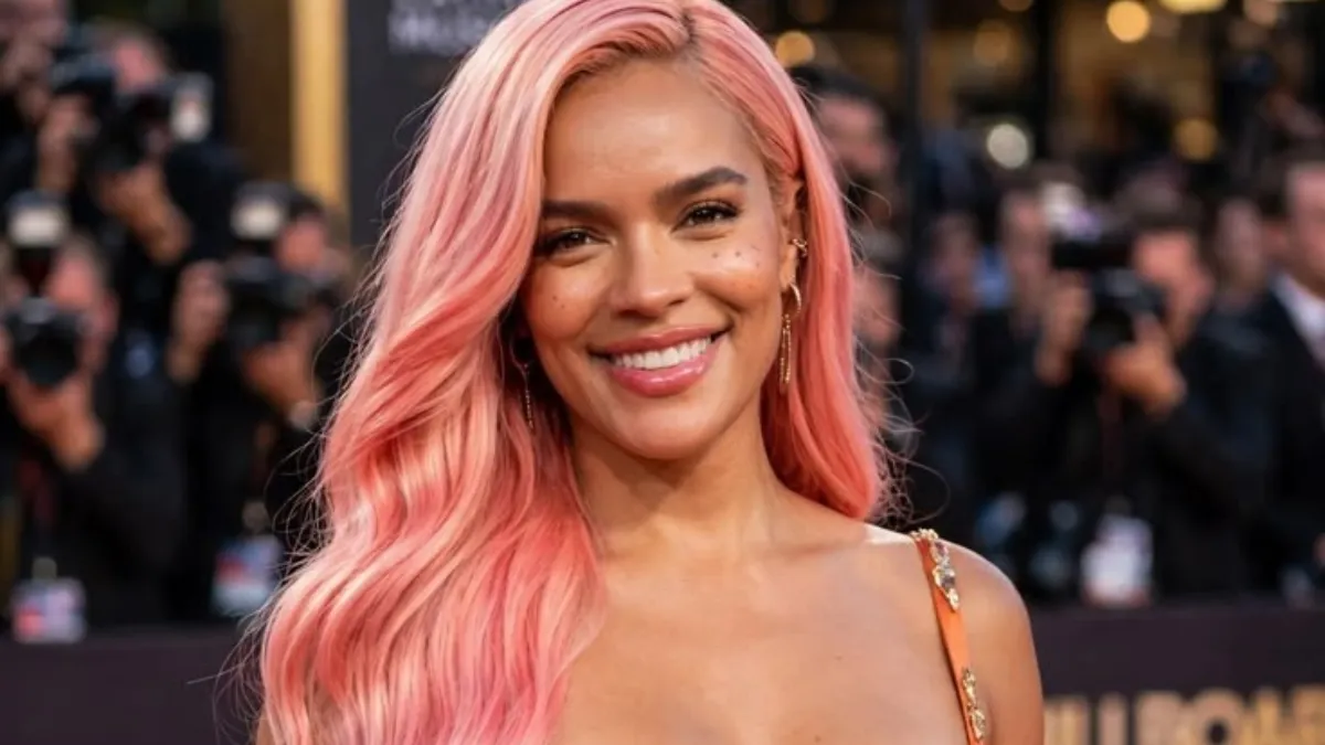 Karol g net worth highlighted in a portrait of Karol G with long pink hair smiling in a burnt orange satin gown at a red carpet event.